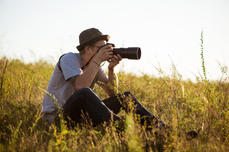 young-male-photographer-hat-taking-picture-sitting-field